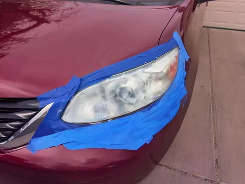Cloudy, yellowed headlight on a red Toyota Sienna, taped off before restoration